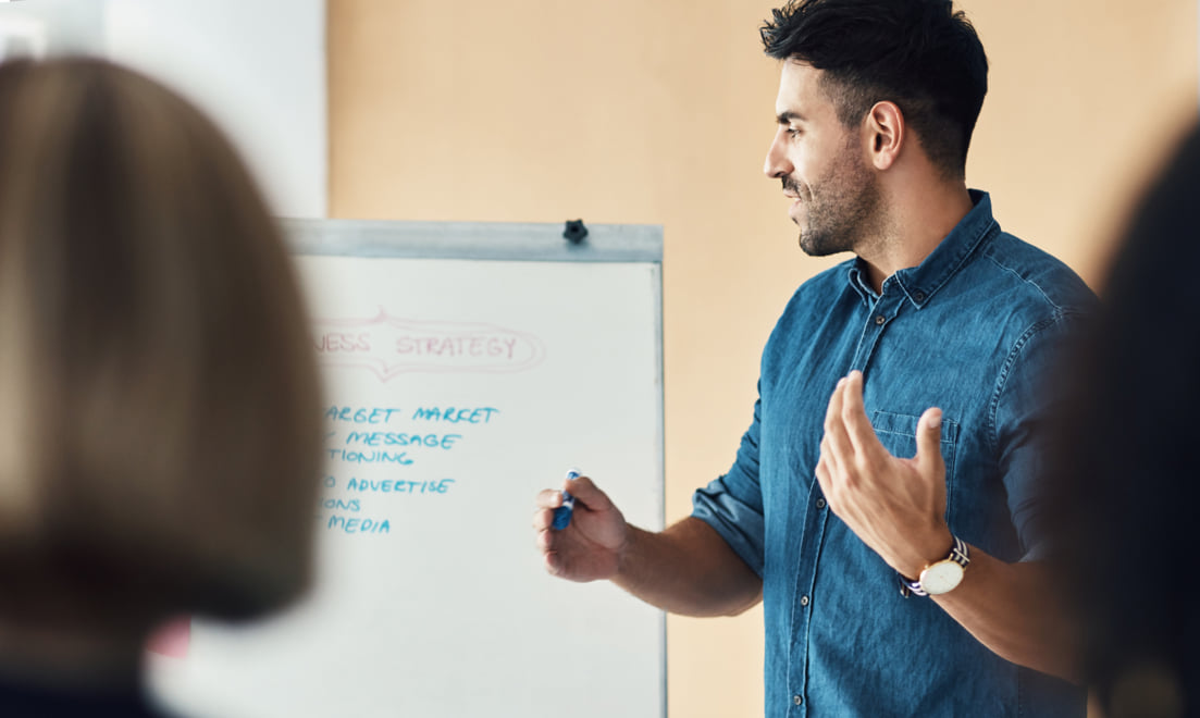 Man standing and writing on a white board during a meeting.
