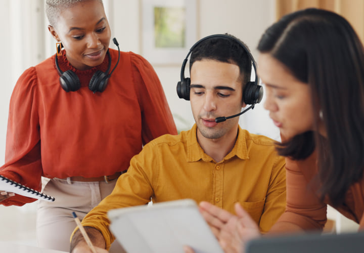 Group of three coworkers wearing headsets and reviewing documents.