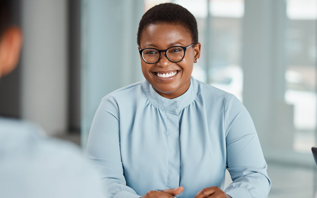 Smiling woman sitting at a desk in a bright office setting.