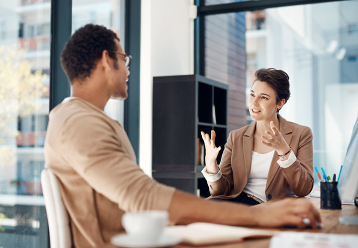 Two coworkers chatting while sitting at a desk.
