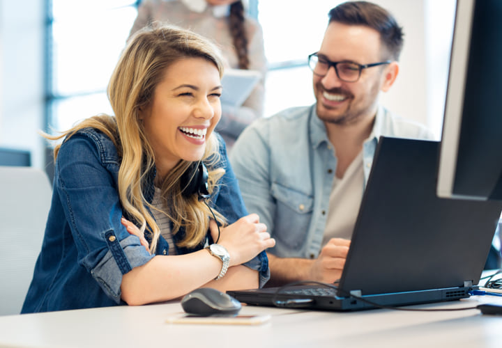 Two smiling coworkers working at a laptop
