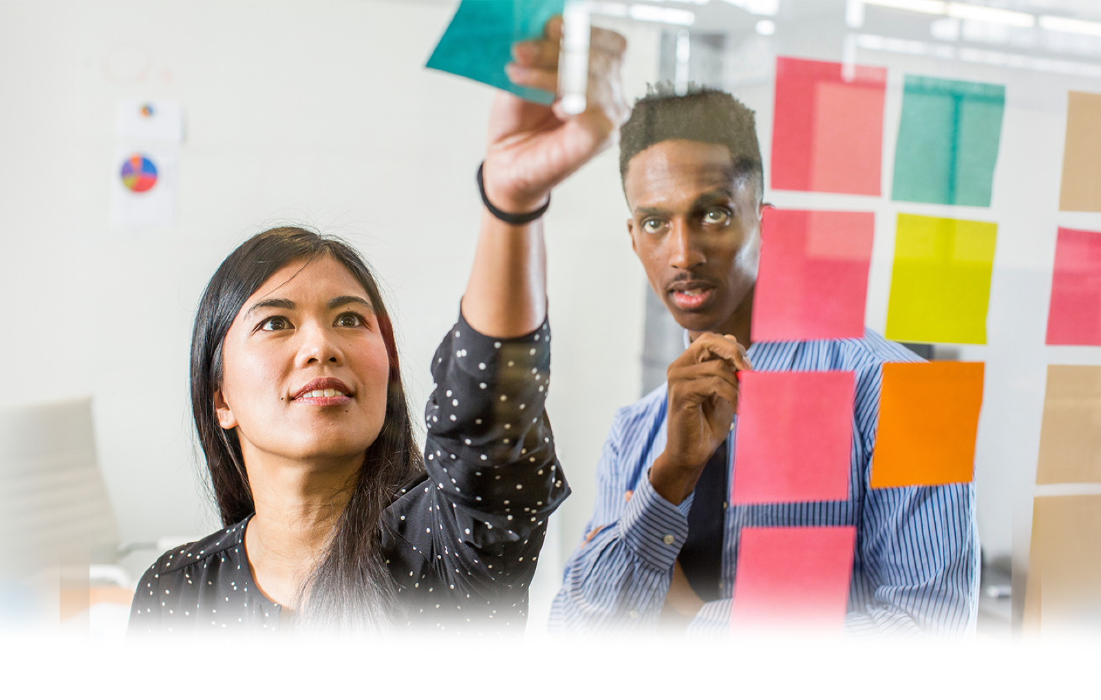 Woman placing colorful sticky it notes on a board in a bright office setting with a blue ‘Inspire a Shared Vision’ banner at the bottom.