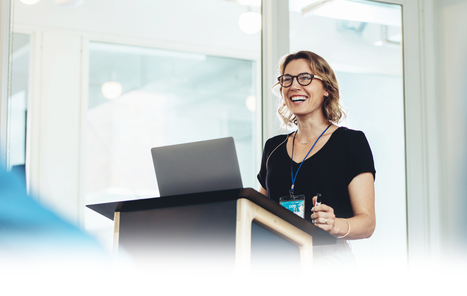 Smiling woman staking in front of a lectern with a green ‘Model the Way’ banner at the bottom.