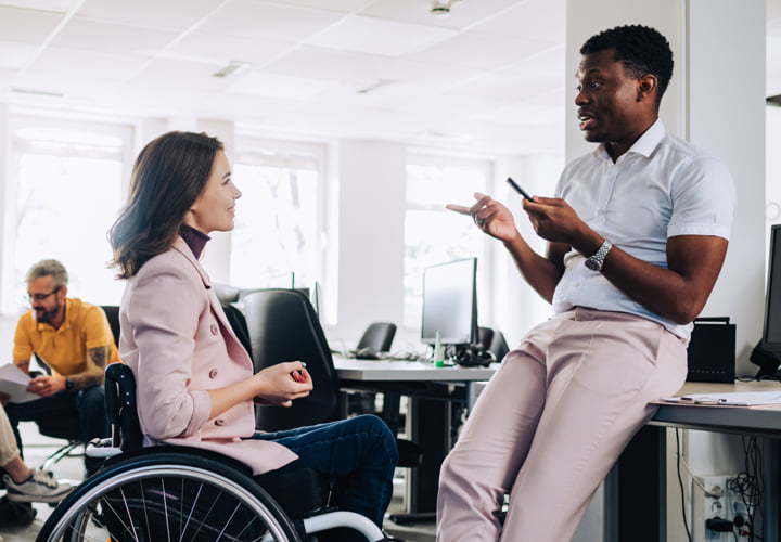 Two coworkers chatting in a bright office setting.