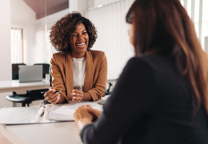 Two coworkers sitting across from each other at a desk, engaged in a discussion.
