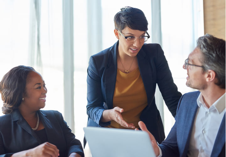 Woman standing a presenting information to two other coworkers.