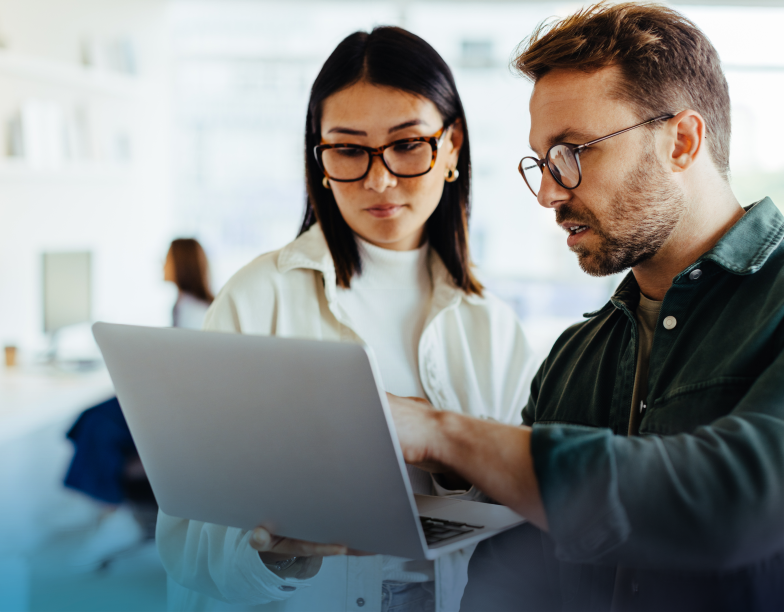 Two coworkers standing while reviewing something on a laptop.